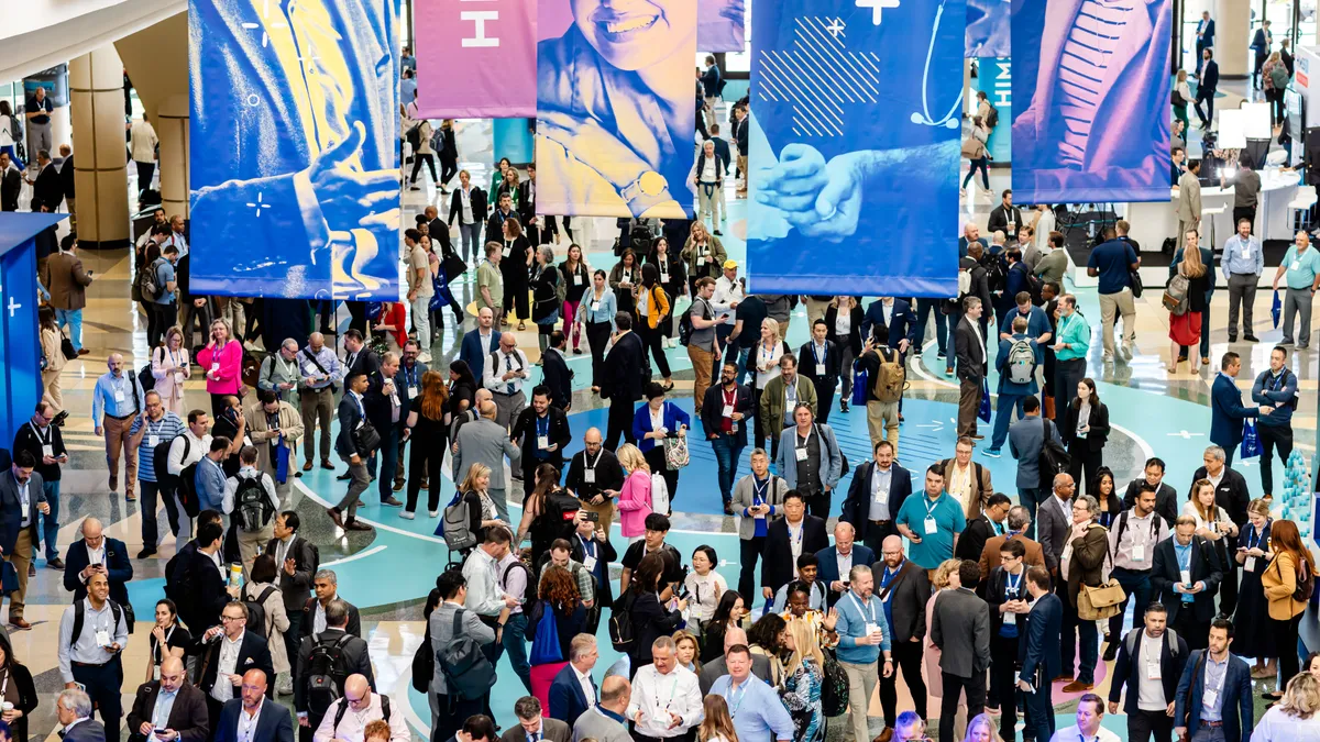 A crowd of conferencegoers under banners emblazoned with the HIMSS24 logo.