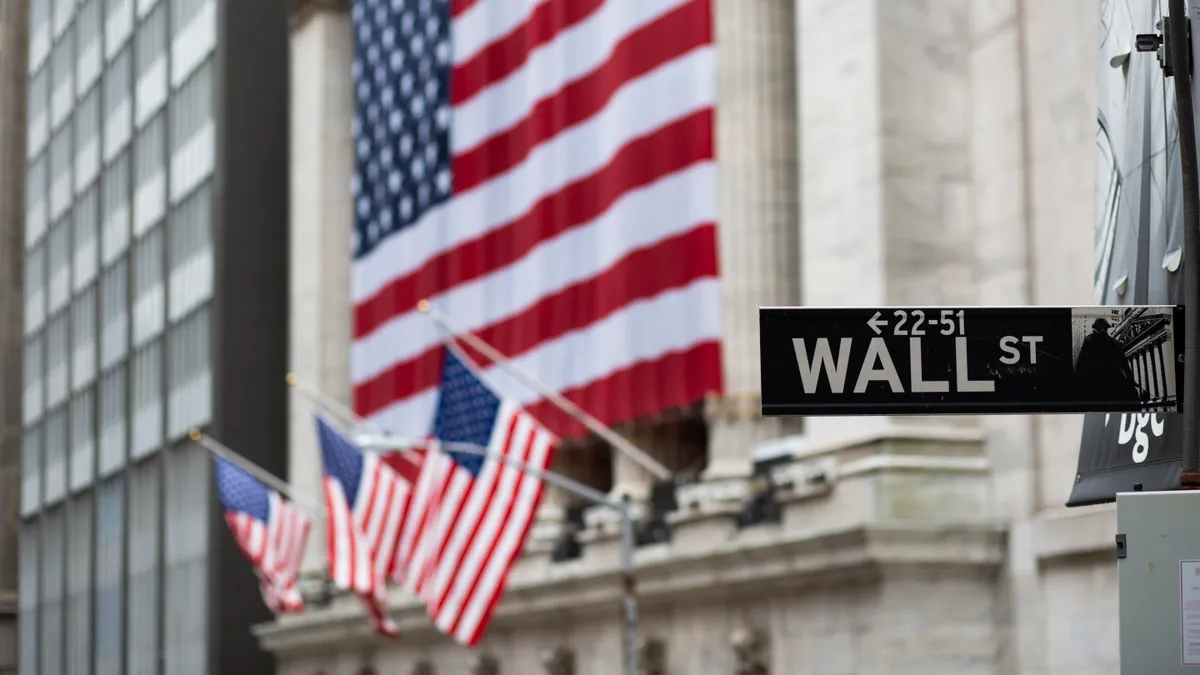 A picture of the street sign stating "Wall Street." American flags drape over a nearby building