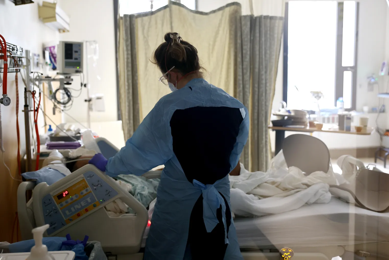 A nurse stands over a patient's bedside in a hospital.