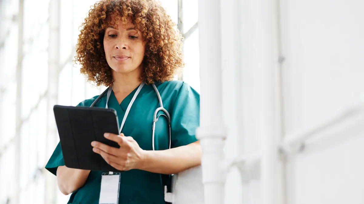 A nurse looks at her tablet by the window.