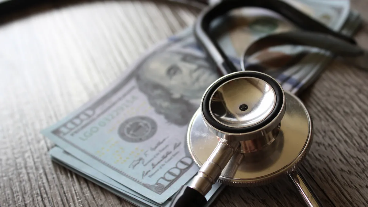 Stethoscope and money on wooden table.