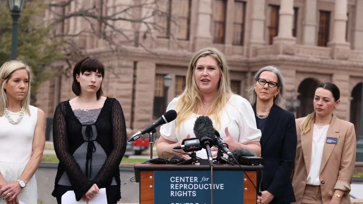 Plaintiffs in the Texas abortion suit stand behind a podium in front of the state capitol.