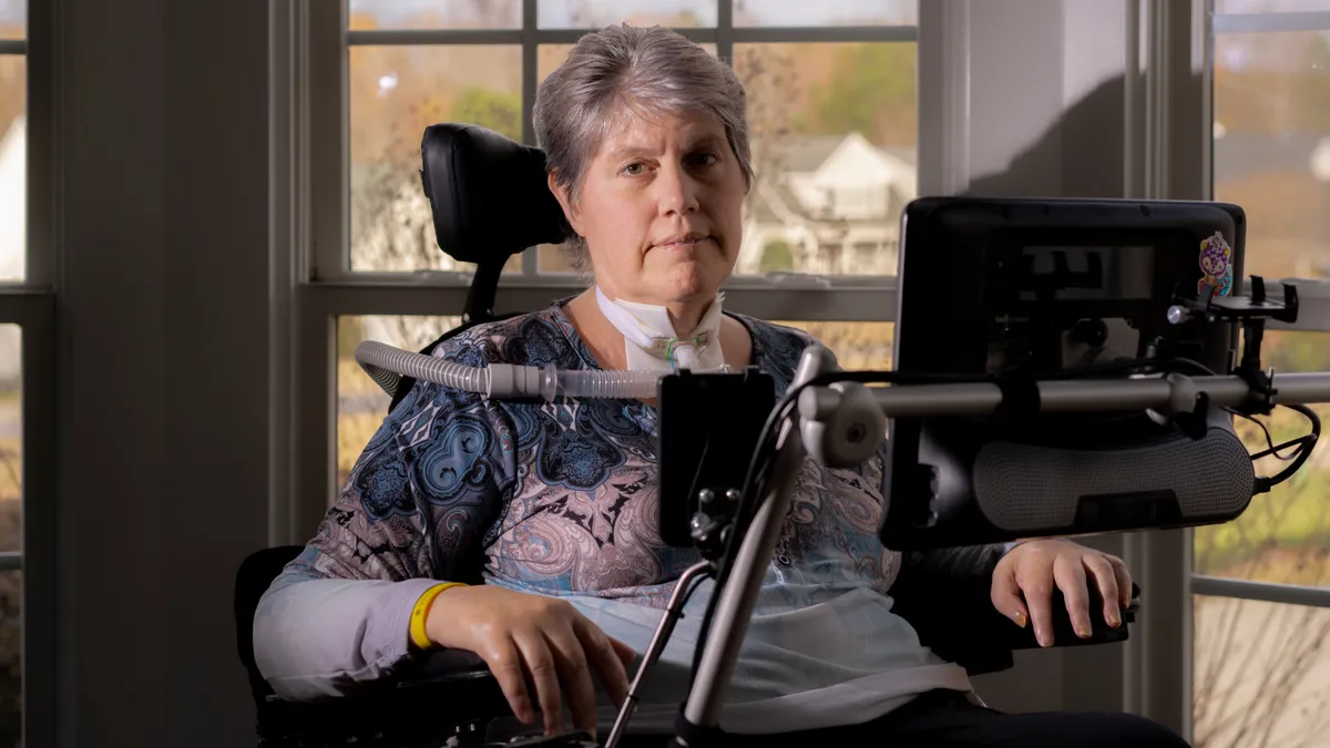 A person sits for a portrait in a room with windows in the background.