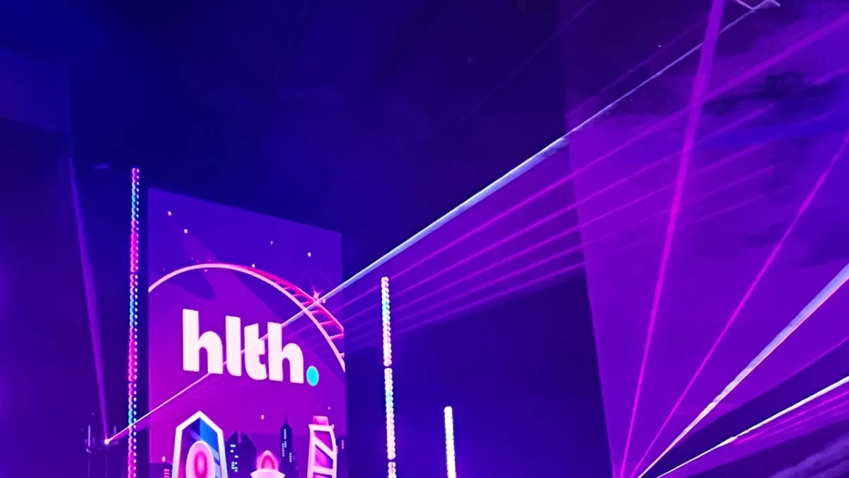 The white HLTH logo on a purple projection screen on the convention floor.